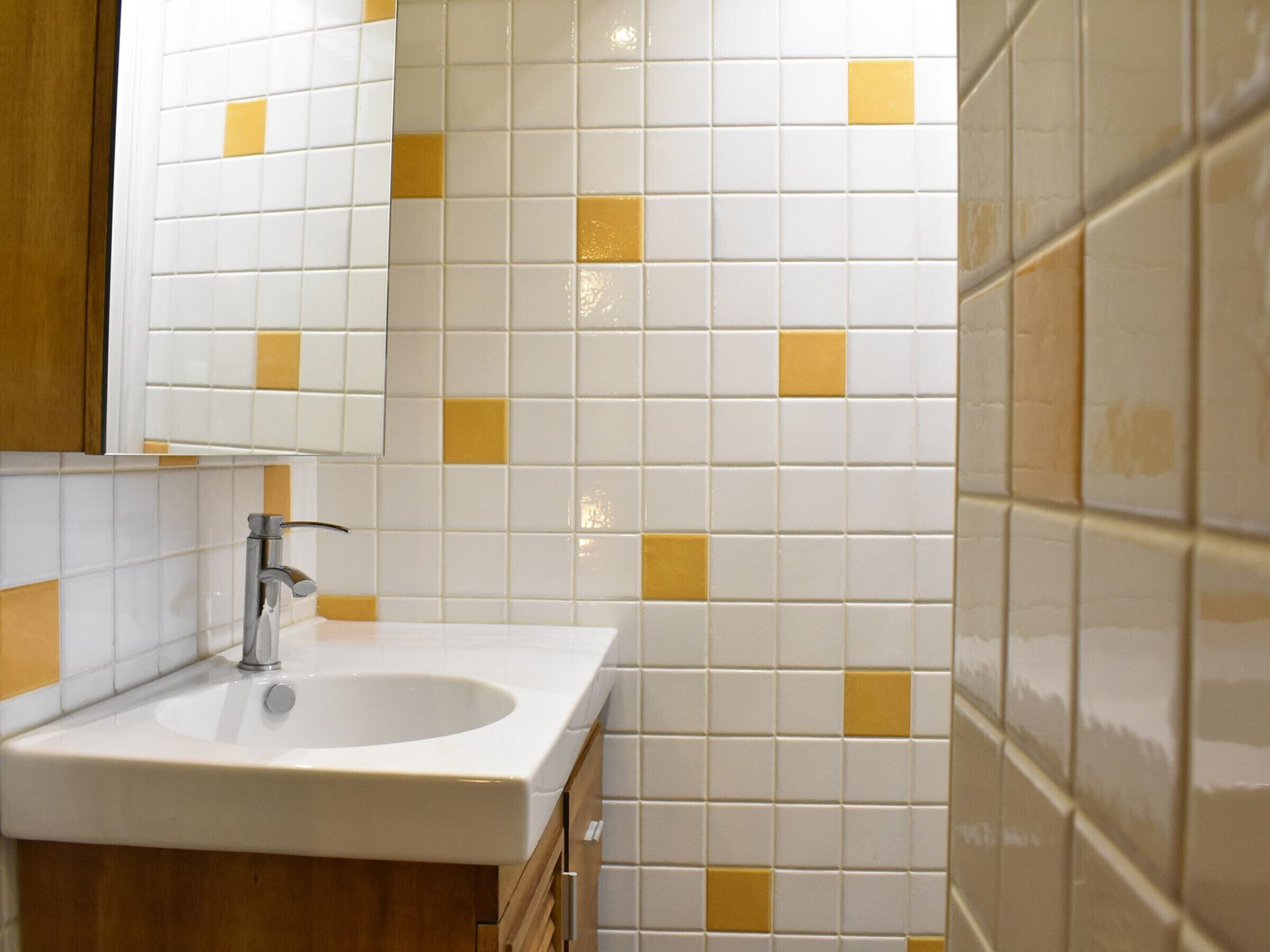 A bathroom with a white sink, wooden cabinets, and tiled walls with yellow accents.