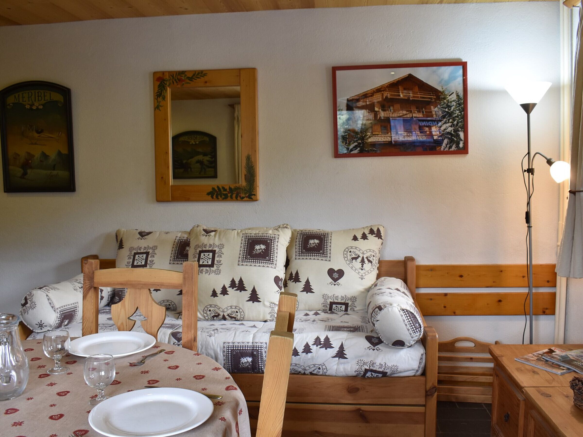 Een gezellige kamer met een houten bed, een eettafel met borden en glazen, een spiegel en een ingelijste foto aan de muur.