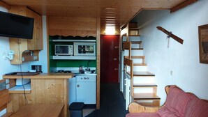 A compact cabin with a kitchenette, a wooden dining table, a sofa, and a staircase. - Cozy studio with mezzanine for 4 people in Arc 1800, near slopes and WiFi included (Les Arcs 1800)