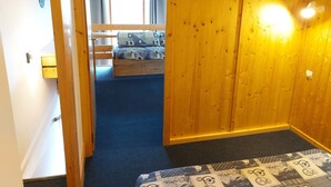 A room with a wooden floor, a bed with patterned bedding, a small table, and a wall-mounted light fixture. - Cozy studio with mezzanine for 4 people in Arc 1800, near slopes and WiFi included (Les Arcs 1800)