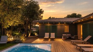 Area piscina con solarium in legno, poltrone a sdraio e una piccola terrazza con tavolo e sedie.