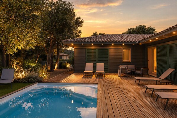 A poolside area with a wooden deck, lounge chairs, and a small patio with a table and chairs. - Villa closed to beaches and mountain with heated pool (Figari)