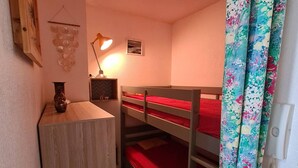 A small, cozy room with bunk beds, a desk, a lamp, and a decorative wall piece.
