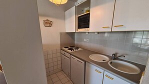 A compact kitchen with white cabinets, a gas stove, a sink, and a small window with a black frame.