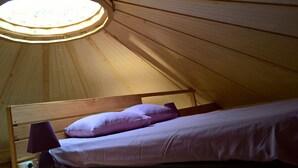 Ein Einzelbett mit Kopfteil und Lampe, ein Dachfenster und Holzwände.