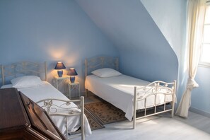 Une chambre avec deux lits simples, une table de chevet avec des lampes, une commode en bois et un tapis à motifs.