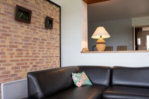 A modern living area with a brick wall, a black leather sofa, a floral cushion, and a lamp on a wooden shelf.