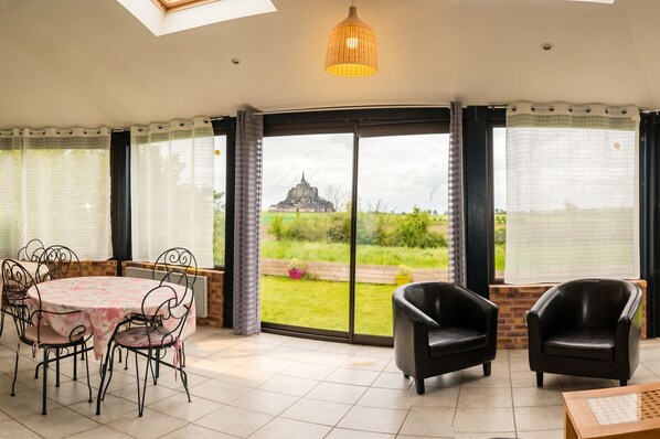 A room with a dining table and chairs, a sofa, and a view of a castle through a glass door.