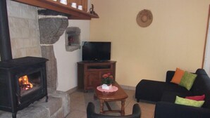 A living room with a stone fireplace, a television, a sofa, and a small table with flowers. - Charming 2-Bedroom House with Garden, BBQ, and Fireplace in Vicq-sur-Mer (Vicq-sur-Mer)