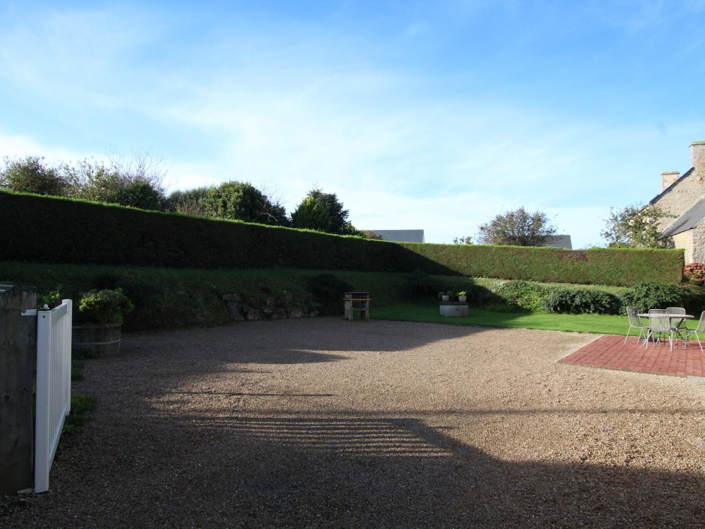 A gravel courtyard with a stone wall, a bench, and a small table with chairs.