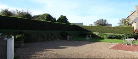 A gravel courtyard with a stone wall, a bench, and a small table with chairs.