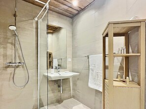 A bathroom with a shower, sink, mirror, and wooden cabinet.