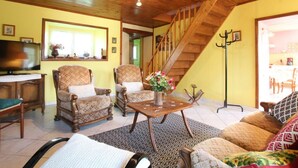 A cozy living room with wooden flooring, a wooden staircase, and a television on a wooden cabinet.
