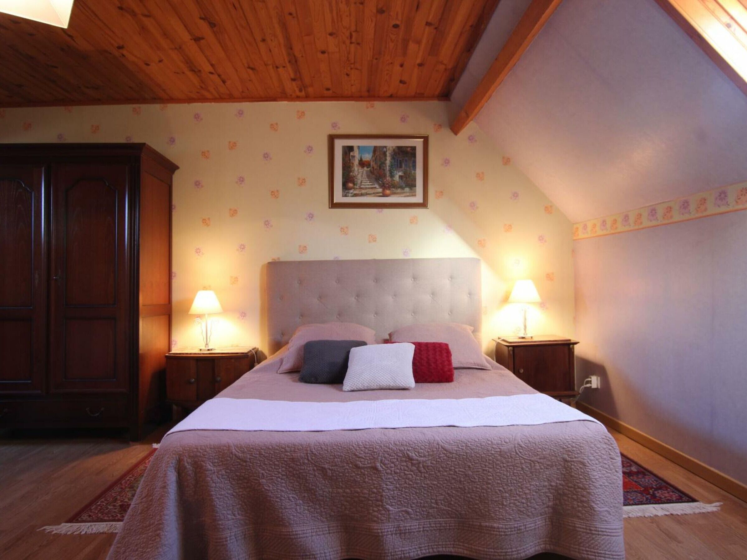 Une chambre à coucher avec un grand lit, deux tables de chevet avec des lampes, une armoire en bois et un papier peint à motifs floraux.