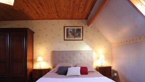 A bedroom with a large bed, two bedside tables with lamps, a wooden wardrobe, and a floral wallpaper pattern.