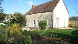 A stone house with a sloped roof, a small garden, and a clear sky.