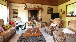 A cozy living room with a fireplace, wooden ceiling, and patterned furniture.