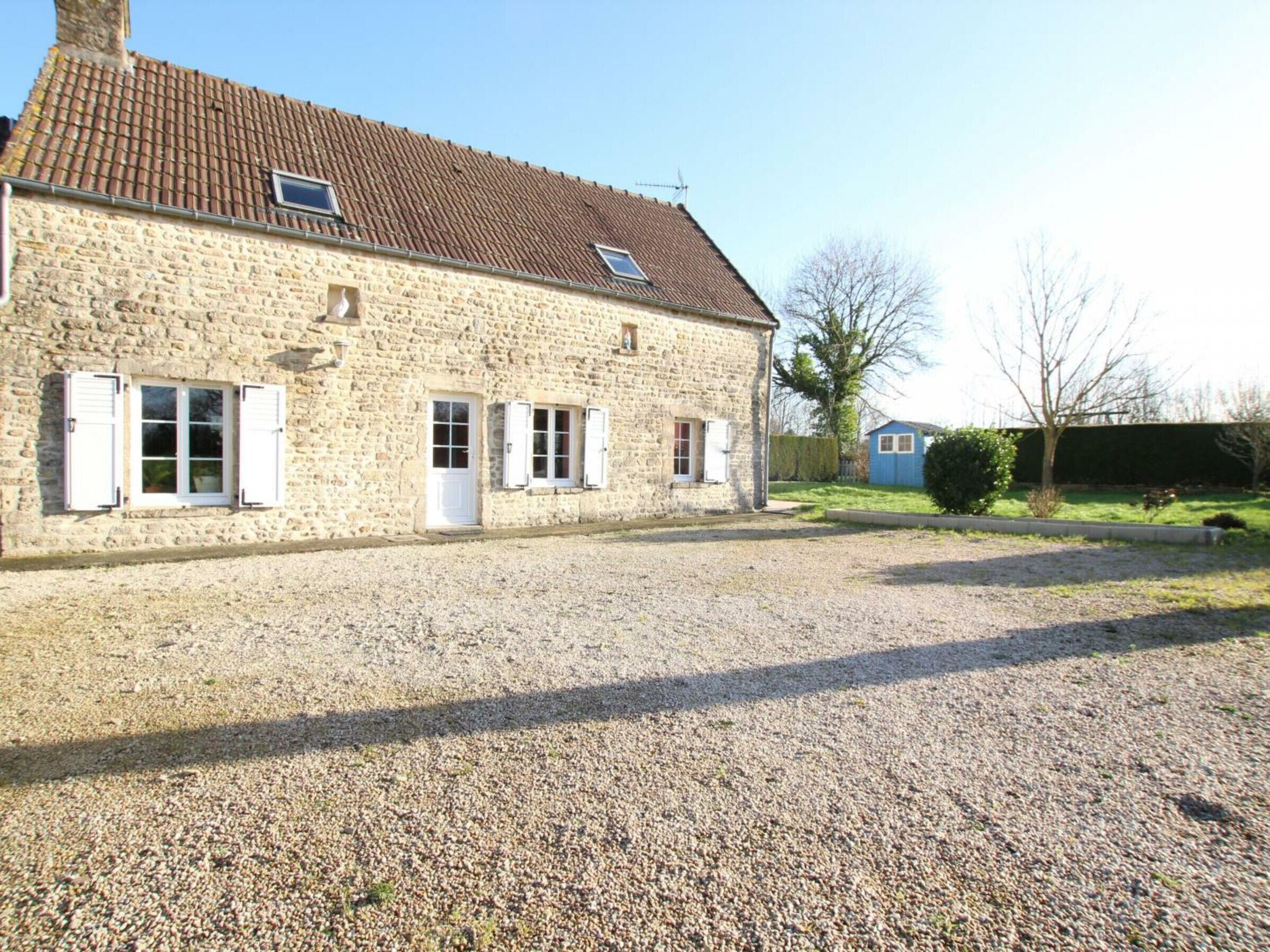 Un bâtiment en pierre avec un toit en tuiles, deux fenêtres avec volets et une allée gravillonnée.