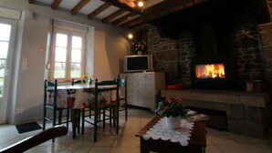 Una sala de estar acogedora con chimenea de piedra, vigas de madera, una mesa de comedor con sillas y un televisor sobre un mueble.