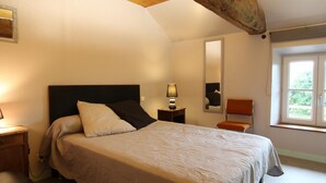 Un dormitorio con cama, mesita de noche, lámpara, silla y ventana con vistas a zonas verdes.