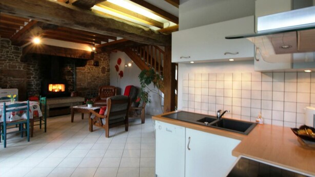 Una sala de estar acogedora con chimenea, vigas de madera, comedor y cocina con alacenas blancas y salpicadero de azulejos.