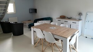 Un soggiorno moderno con angolo pranzo, TV a parete, una scala e un frigorifero.