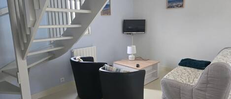 A modern living room with a white spiral staircase, a flat-screen TV, a small table with a lamp, and a grey sofa.