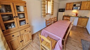 Une cuisine de taille réduite, dotée de meubles en bois, d’une table à manger recouverte d’une nappe à carreaux et d’un four à micro-ondes.