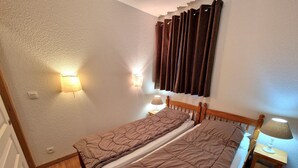 Une petite chambre avec un lit simple, une tête de lit en bois, deux tables de chevet avec des lampes et un rideau fixé au mur.