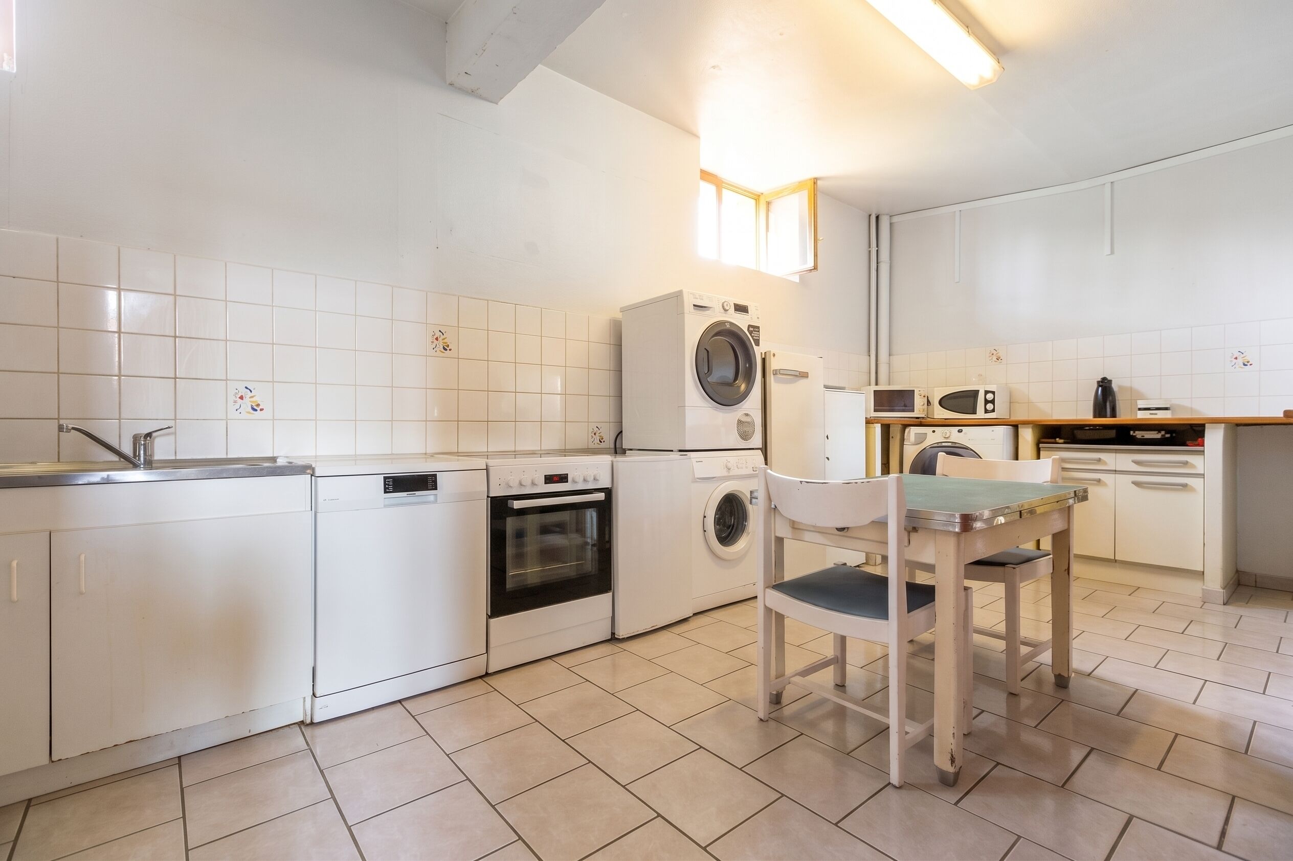 Eine kompakte Küche mit Waschmaschine, Backofen, Mikrowelle und einem Essbereich mit Tisch und Stuhl.