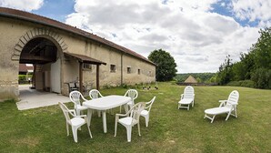 Une terrasse extérieure avec une table et des chaises, un espace abrité et un bâtiment doté d’une arche en pierre.