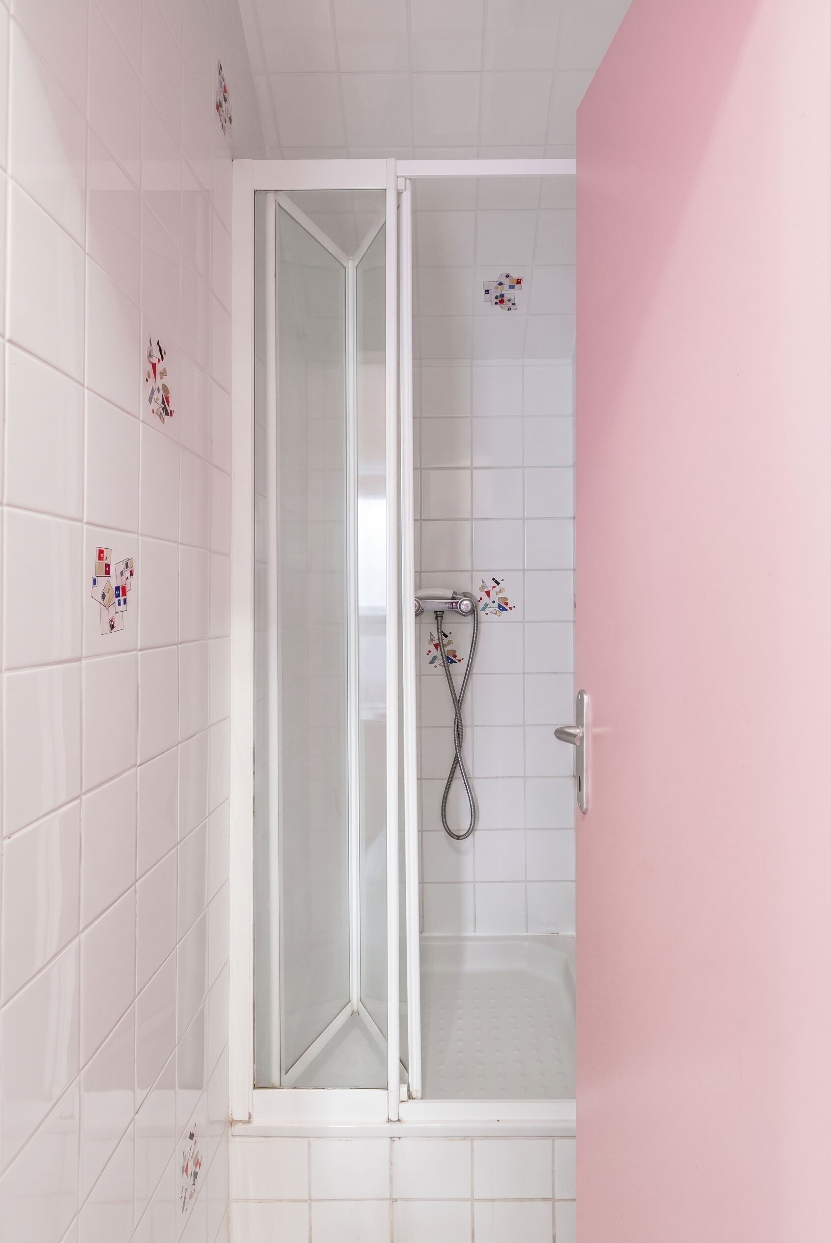 Een douche met een glazen deur, witte betegelde wanden en een roze muur.
