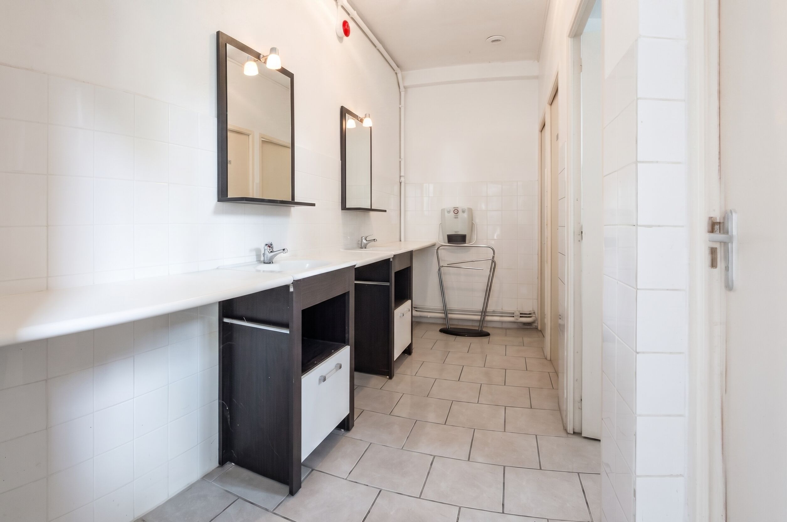 Een moderne badkamer met een betegelde muur, een dubbele wastafel, een spiegel en een handdoekrek.