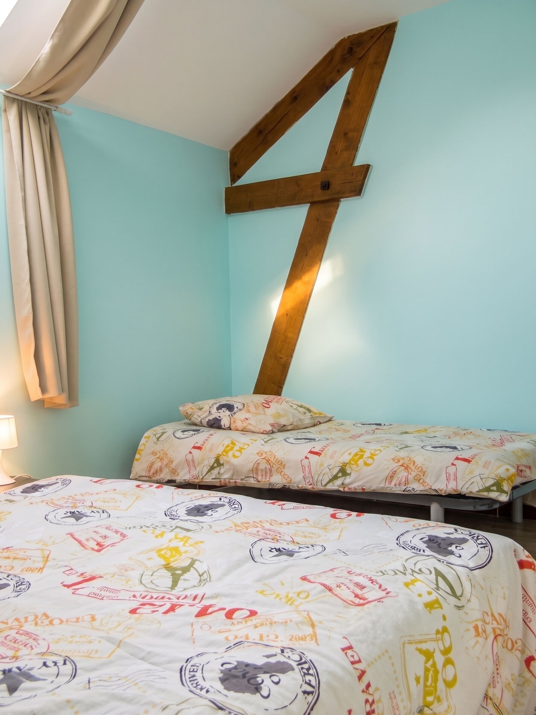 Een kamer met twee bedden, een houten balk aan de muur en een lichtgekleurd gordijn.