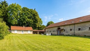 Un bâtiment avec un toit recouvert de tuiles, une pelouse verdoyante et un grand arbre en arrière-plan.