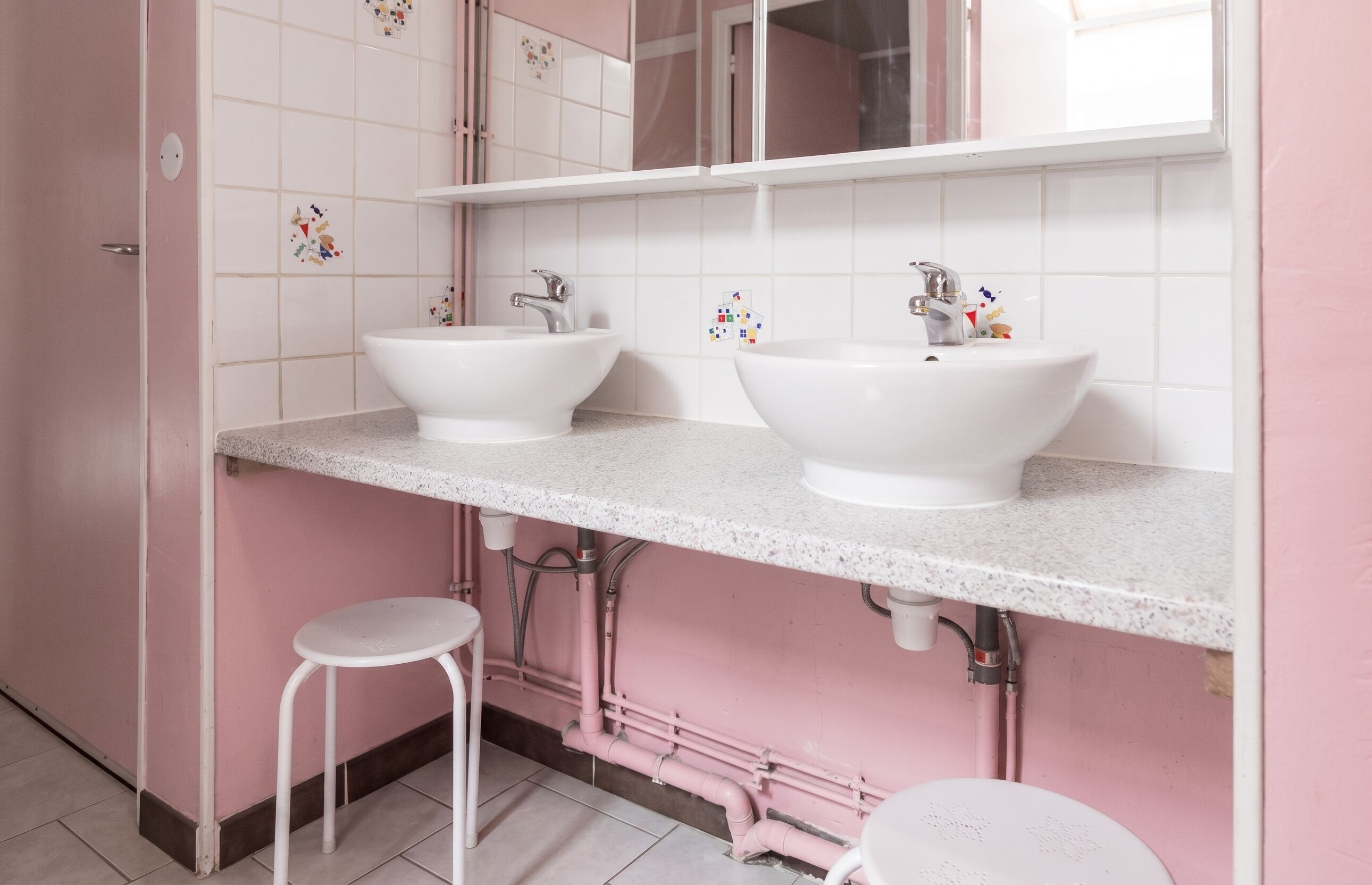 Een badkamer met twee witte wasbakken, een spiegel en een roze wand.