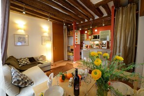 A cozy living room with a sofa, a dining table with a bottle of wine, and a vase of flowers. - B1DD Browning (París)
