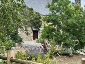 Un bâtiment en pierre avec une porte en bois, entouré de différentes plantes et arbres.