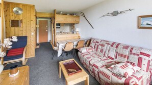 Interior acolhedor de cabana com área de jantar de madeira, um sofá com capa estampada em vermelho e branco e uma pequena mesa de madeira com um livro e uma xícara.