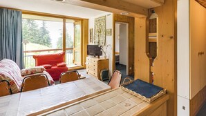Interior acolhedor de uma cabana, com área de jantar, televisão e vista para o exterior.