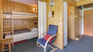 Quarto de cabana de madeira com beliches, uma cadeira de balanço e um pequeno armário de madeira.