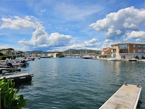 A marina with boats docked, a wooden pier, and buildings with balconies.