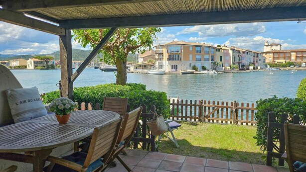 Une terrasse avec une table et des chaises, une vue sur un lac et des bâtiments en arrière-plan.