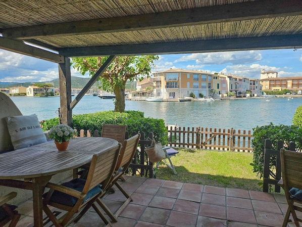 A terrace with a table and chairs, a view of a lake, and buildings in the background.