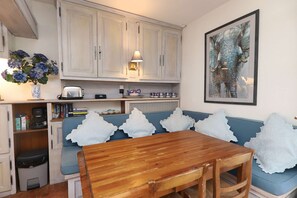 A compact kitchen with white cabinets, a wooden dining table, a blue sofa with white pillows, and a framed elephant painting on the wall.