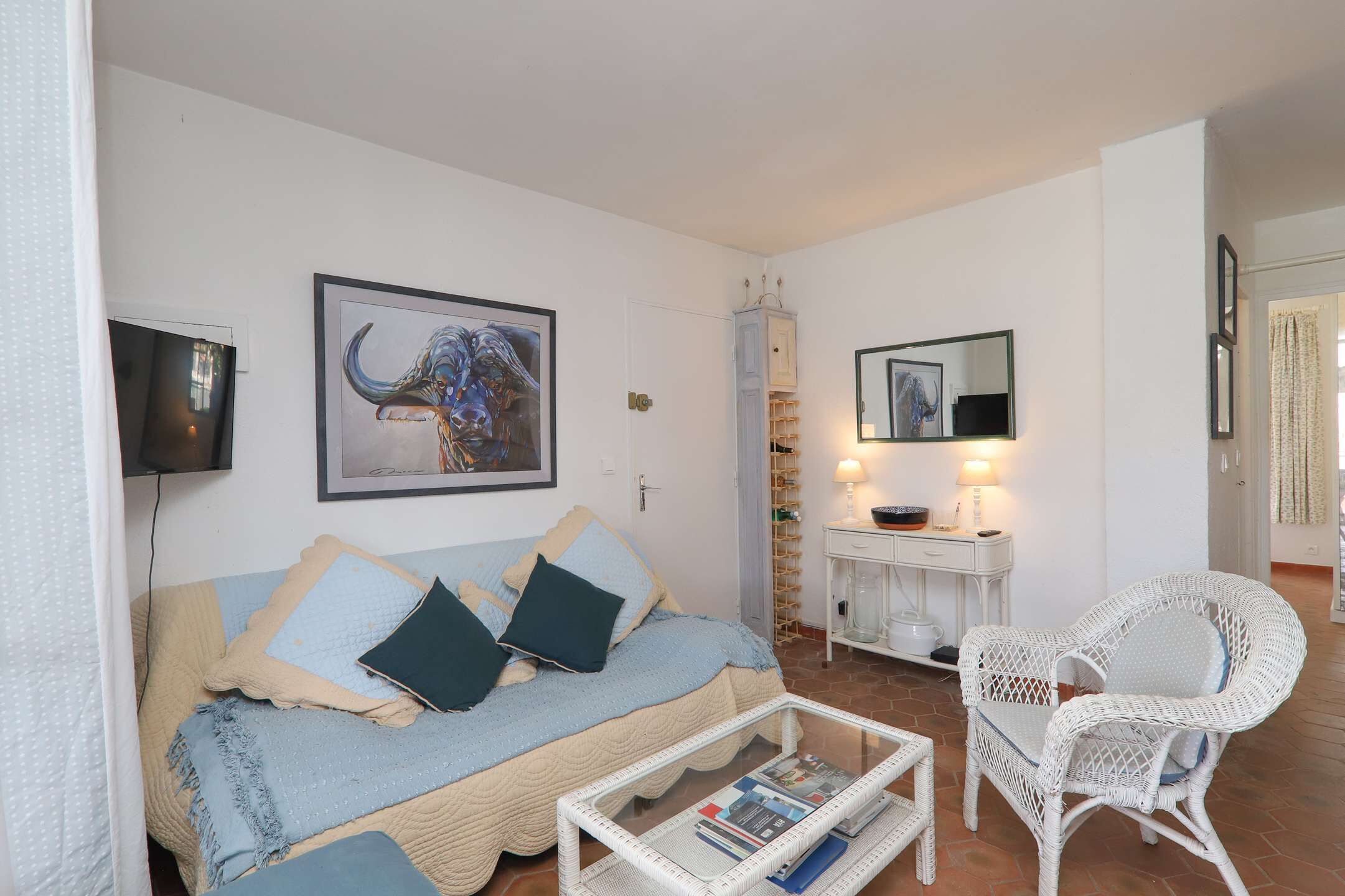 Un salon comprenant un canapé, un fauteuil en osier, une table basse, un meuble et un téléviseur.