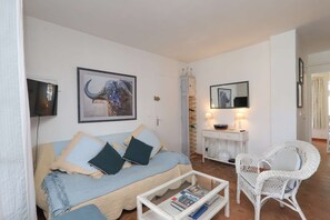A living room with a sofa, a wicker chair, a coffee table, a cabinet, and a television.