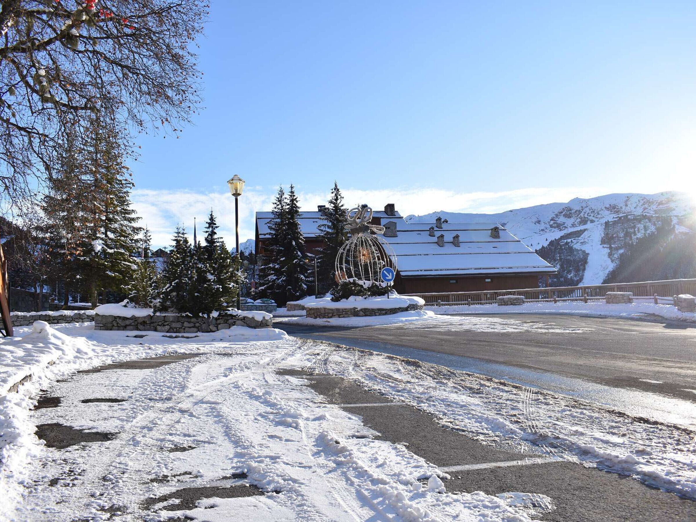 A snow-covered landscape with a building featuring a traditional chalet style, surrounded by snow-laden trees and a clear sky.
