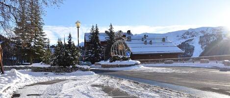 A snow-covered landscape with a building featuring a traditional chalet style, surrounded by snow-laden trees and a clear sky.