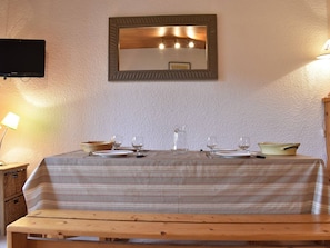 Un comedor con una mesa dispuesta para dos personas, un espejo arriba y un televisor en la pared.